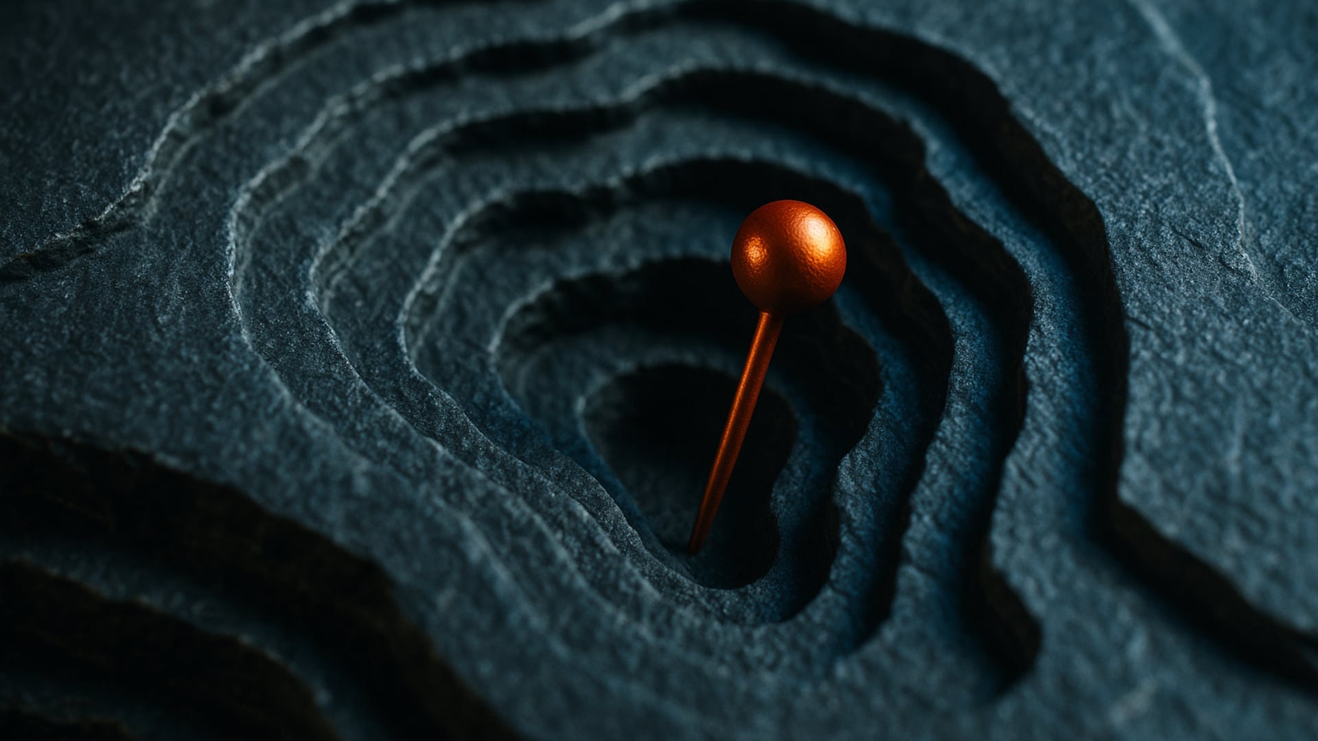 Tactile 3D rendering of a deeply carved, terraced topographical map made of dark, porous slate, with a single, brilliant burnt-orange (#c4571c) metallic pin resting exactly at the deepest point of a